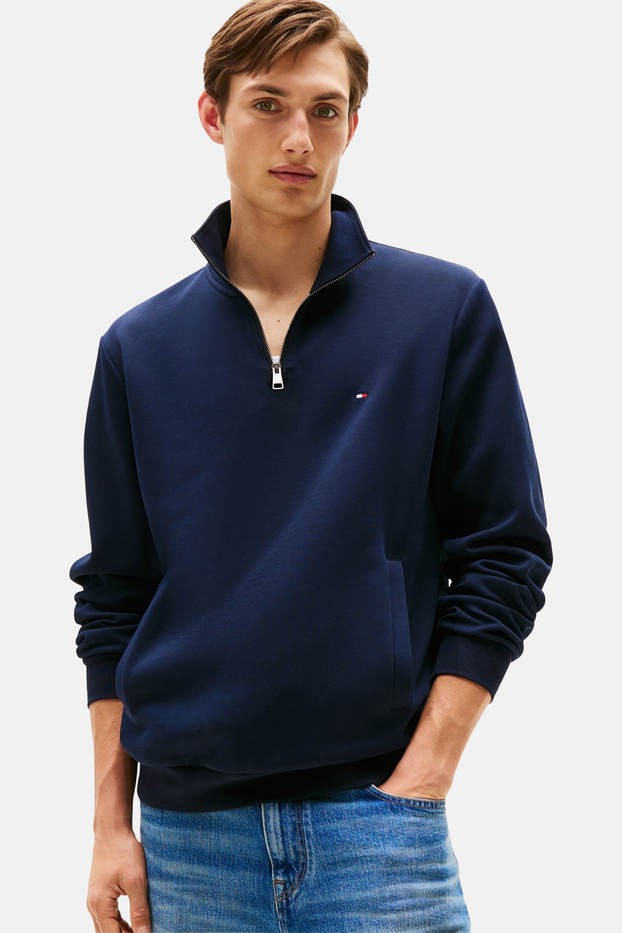 Sweat bleu foncé à col zippé de Tommy Hilfiger, porté avec un jean délavé et mains dans les poches.