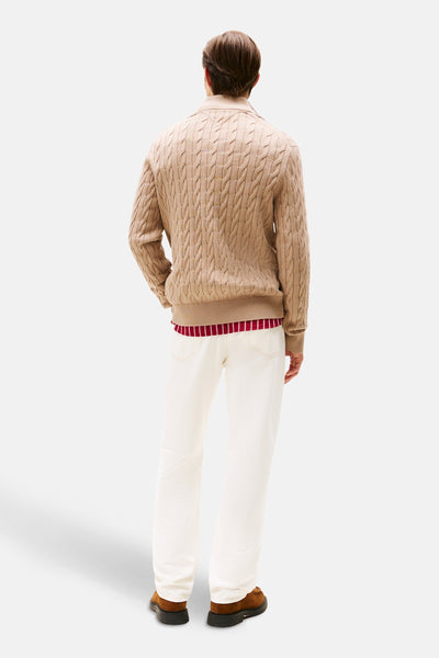 Pull à col roulé beige de TOMMY HILFIGER avec torsades, porté avec un t-shirt rayé et un pantalon blanc, vue de dos.