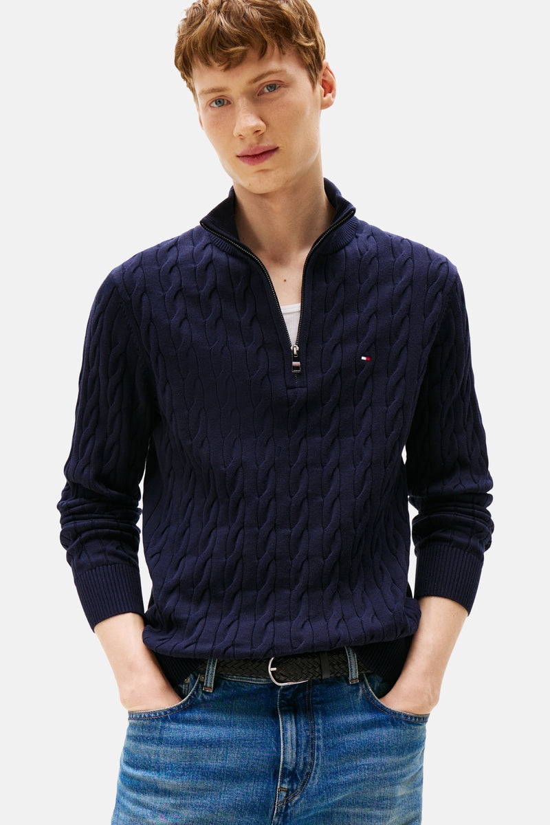 Donkerblauwe coltrui van Tommy Hilfiger, in kabelsteek, gedragen met een spijkerbroek en een gevlochten riem.