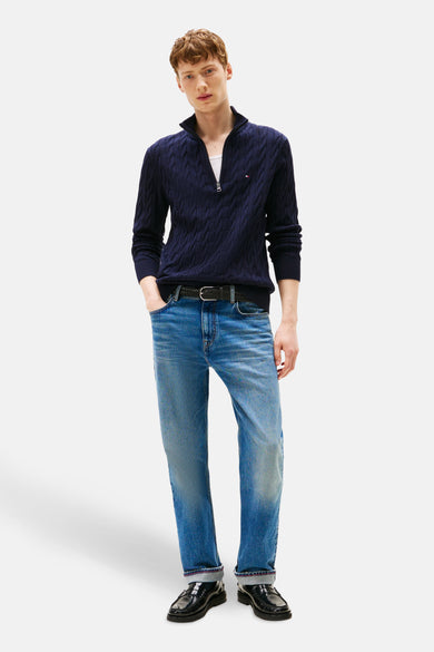 Blauwe trui met ritssluiting van Tommy Hilfiger, met een kabelpatroon, gedragen met een spijkerbroek en zwarte loafers.