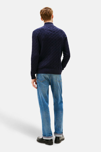 Blauwe coltrui van TOMMY HILFIGER, met een kabelpatroon, gedragen met een spijkerbroek en zwarte loafers.