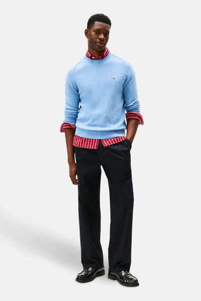 Ronde hals trui blauw van TOMMY HILFIGER, gedragen over een rood-wit gestreept overhemd, met een donkere broek en zwarte loafers.