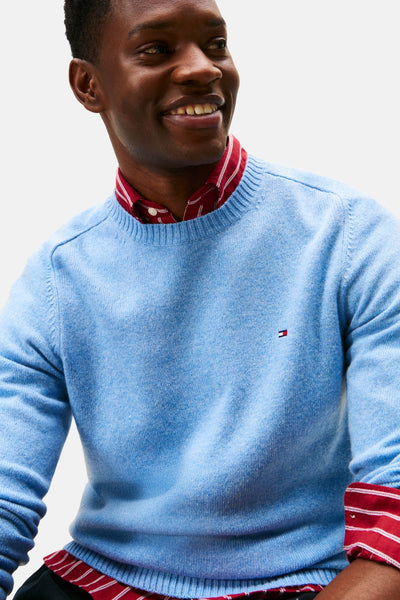 Pull en tricot bleu de TOMMY HILFIGER, porté sur une chemise rayée rouge et blanche.