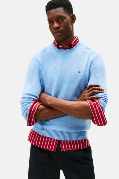 Blauwe trui met ronde hals van TOMMY HILFIGER, gedragen over een rood-wit gestreept overhemd.