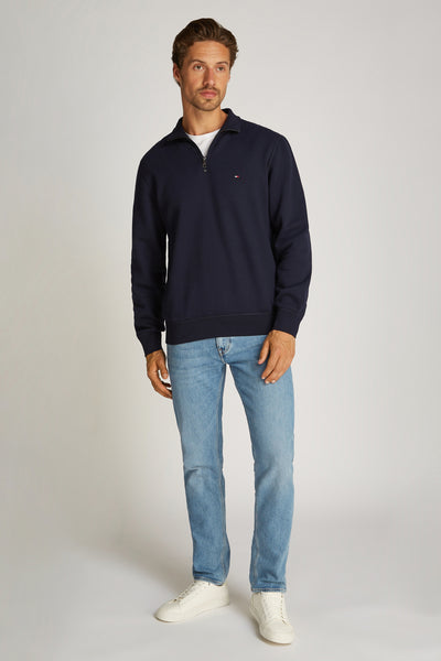 Blauwe sweater met opstaande kraag van Tommy Hilfiger, gedragen met een wit T-shirt, een casual spijkerbroek en witte sneakers.