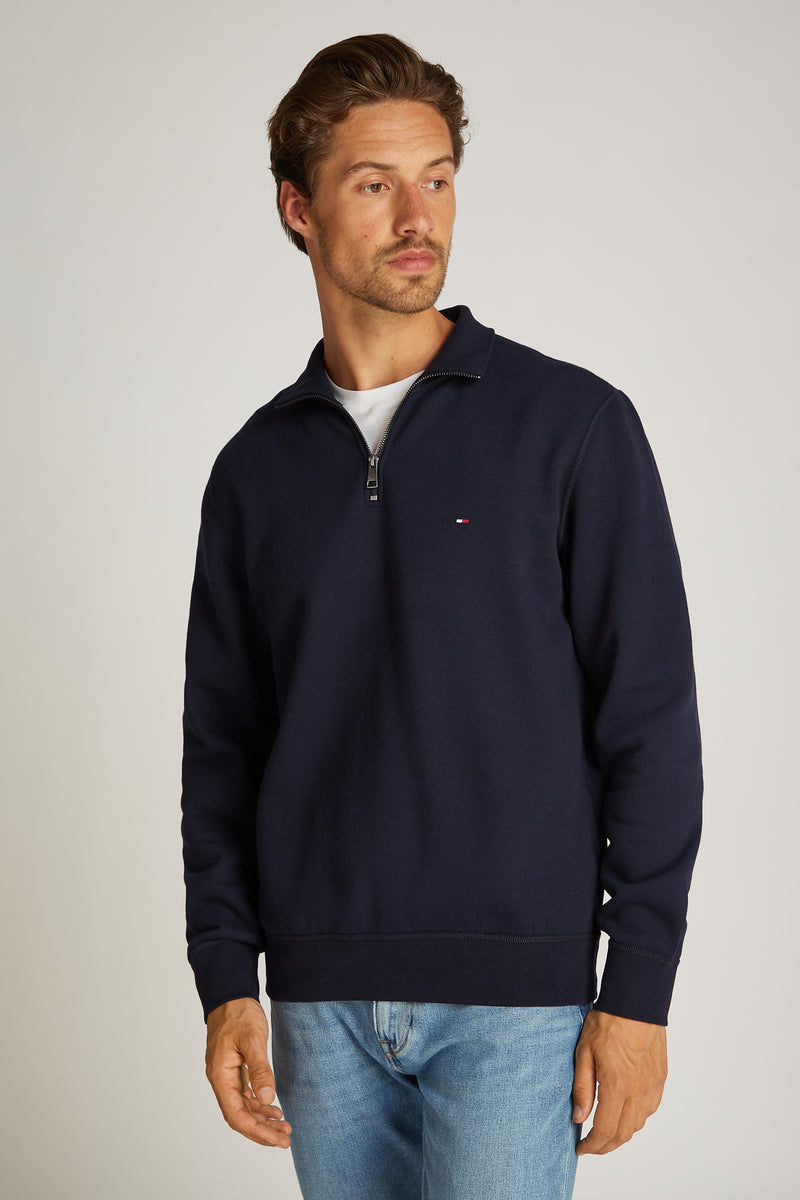 Blauwe sweater met opstaande kraag van Tommy Hilfiger, met ritssluiting en gedragen met een wit T-shirt en een blauwe jeans.