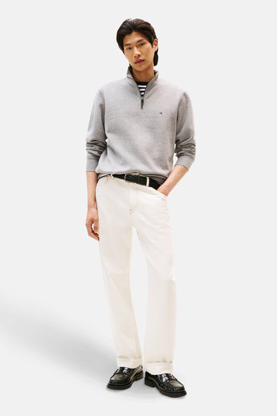 Grijze sweater met opstaande kraag van Tommy Hilfiger, gedragen over een gestreept T-shirt, met een witte broek en zwarte loafers.