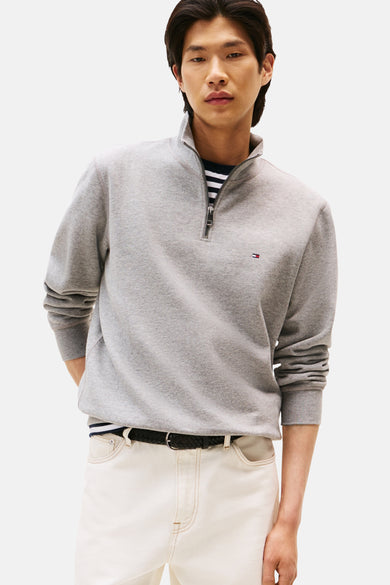 Grijze sweater met opstaande kraag van TOMMY HILFIGER, gedragen over een gestreept T-shirt, met een witte broek en een gevlochten riem.