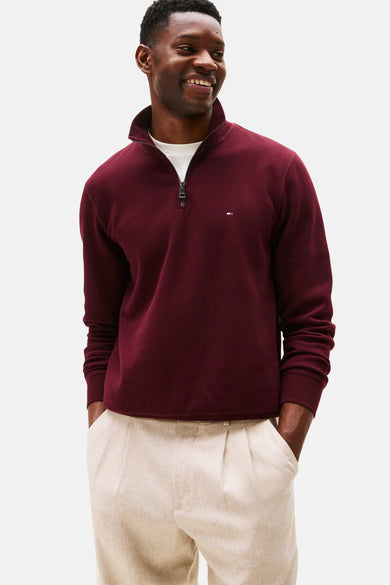 Bordeauxrode trui met opstaande kraag van Tommy Hilfiger, gedragen over een wit T-shirt en een beige broek.