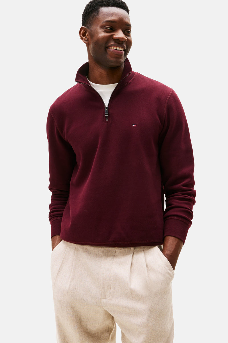 Bordeauxrode trui met opstaande kraag van Tommy Hilfiger, gedragen over een wit T-shirt en een beige broek.