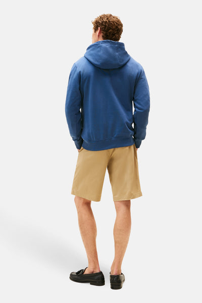 Blauwe hoodie van TOMMY HILFIGER, gedragen met een beige korte broek en zwarte loafers, achterzijde.