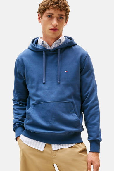 Blauwe hoodie van TOMMY HILFIGER, gedragen over een gestreept overhemd, met een beige chino broek.
