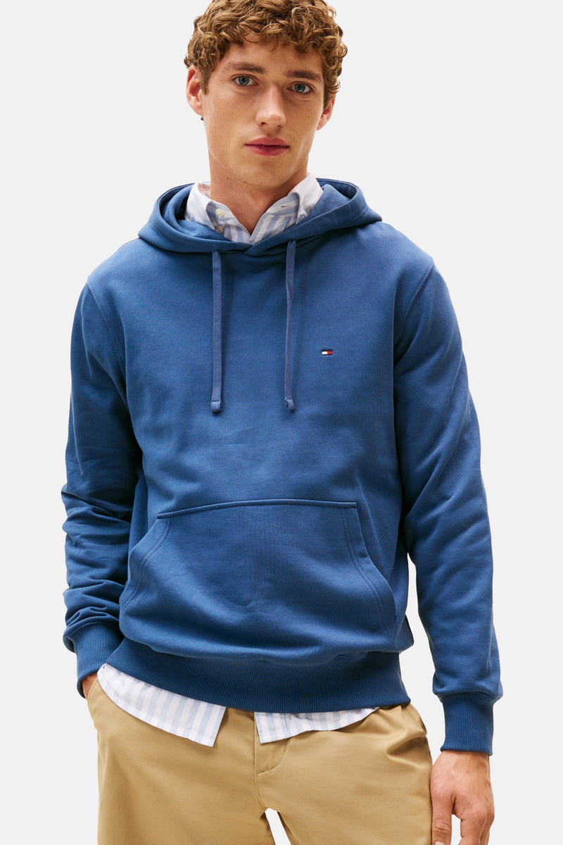 Blauwe hoodie van TOMMY HILFIGER, gedragen over een gestreept overhemd, met een beige chino broek.
