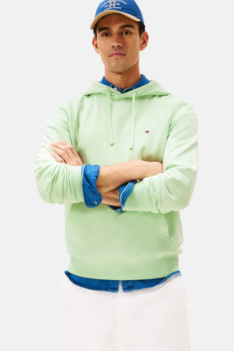 Sweat à capuche vert de Tommy Hilfiger, porté avec une chemise en jean et une casquette bleue.