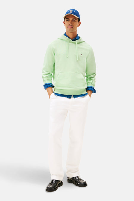 Sweat à capuche vert clair de Tommy Hilfiger, porté sur une chemise en jean et un pantalon blanc, avec casquette bleue.
