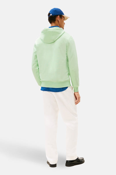 Sweat à capuche vert de TOMMY HILFIGER, porté avec un pantalon blanc et des chaussures noires.