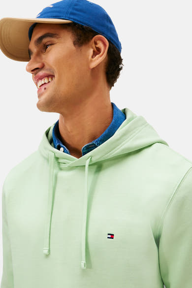 Sweat à capuche vert de TOMMY HILFIGER, porté sur une chemise en jean et sous une casquette bleue.