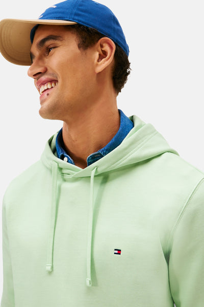 Groene hoodie van TOMMY HILFIGER, gedragen over een spijkerhemd en onder een blauwe pet.