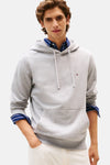 Grijze Tommy Hilfiger hoodie met trekkoord, gedragen over een blauw gestreept overhemd en een witte jeans.