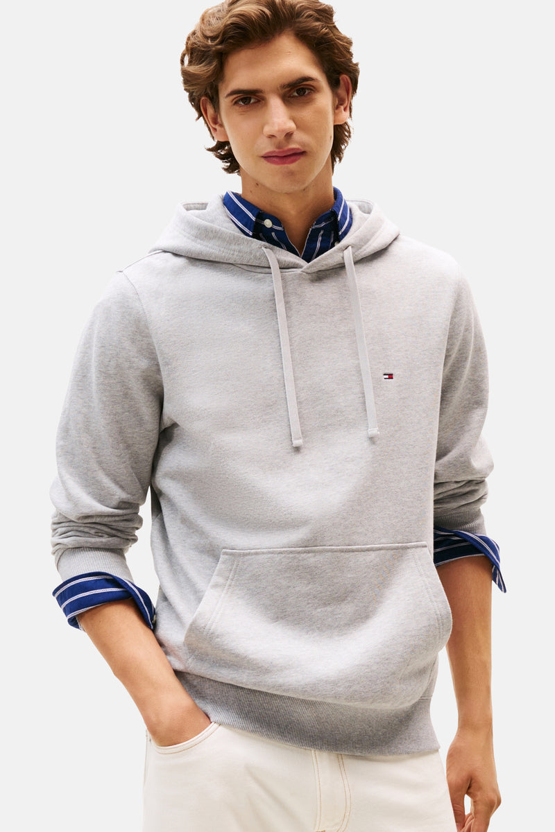 Grijze Tommy Hilfiger hoodie met trekkoord, gedragen over een blauw gestreept overhemd en een witte jeans.