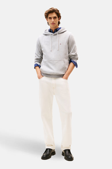 Sweat à capuche gris de Tommy Hilfiger avec cordon de serrage, porté sur une chemise rayée bleue et un jean blanc.