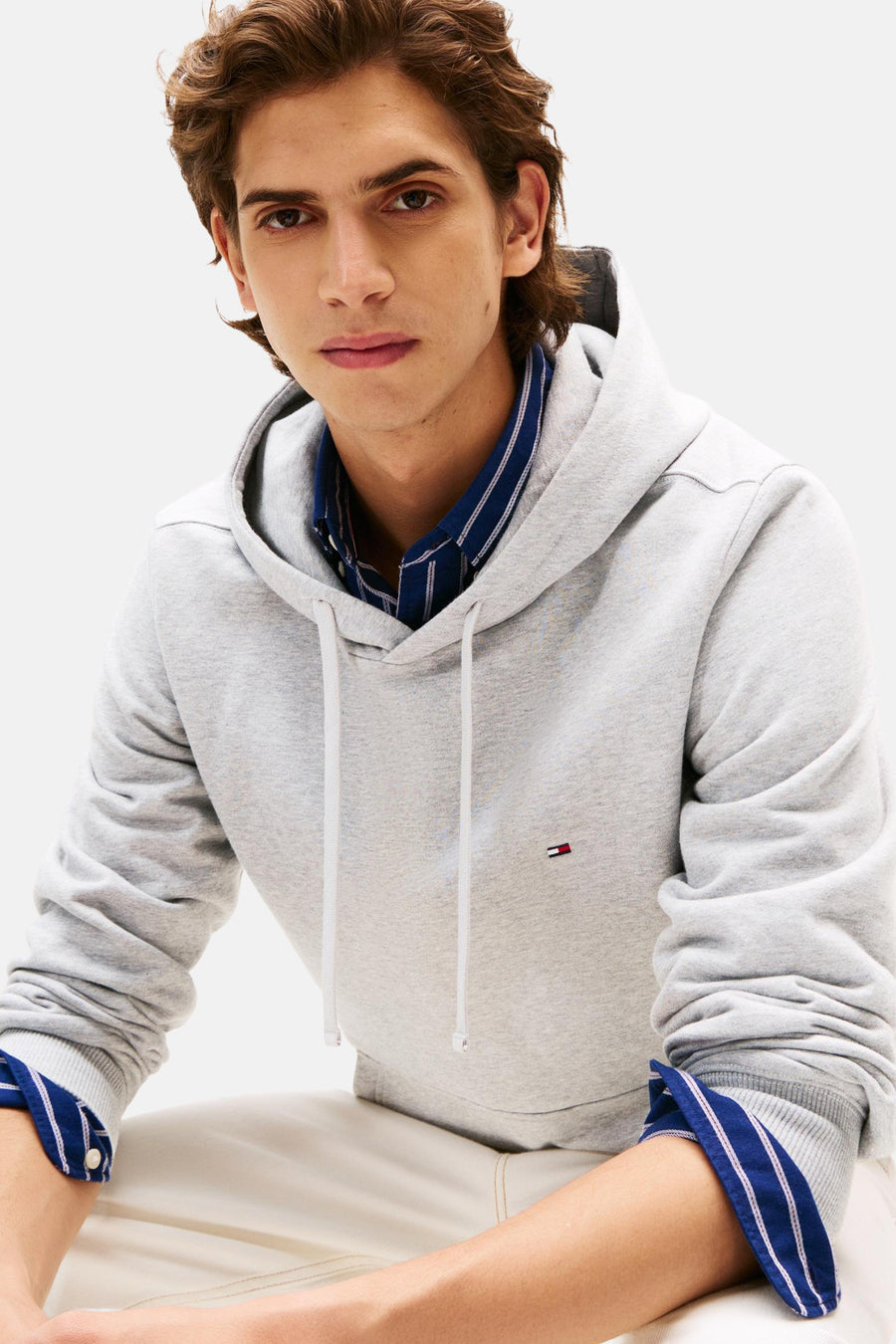 Grijze hoodie van TOMMY HILFIGER met trekkoord, gedragen over een blauw-wit gestreept overhemd.