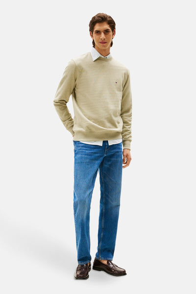 Groene sweater van TOMMY HILFIGER, gedragen over een wit gestreept overhemd, met een blauwe jeans en bordeauxrode leren loafers.