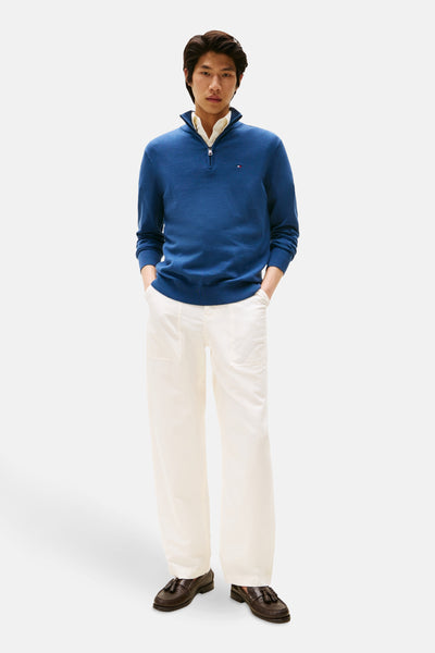 Pull à col roulé bleu par TOMMY HILFIGER, porté avec une chemise et un pantalon blanc cassé.