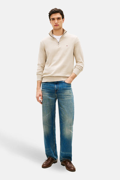 Pull à col roulé beige de TOMMY HILFIGER, porté avec un t-shirt blanc et un jean bleu délavé, avec des chaussures marron.