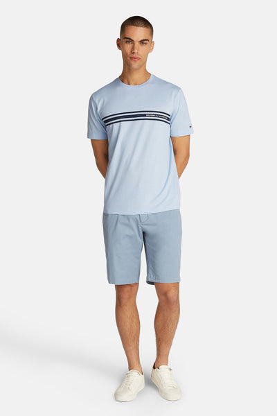 T-shirt à manches courtes bleu de TOMMY HILFIGER, avec rayures horizontales et porté avec un short bleu et des baskets blanches.
