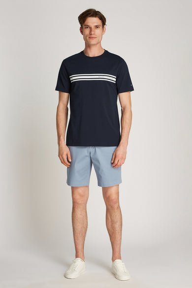 T-shirt bleu à manches courtes de TOMMY HILFIGER, avec trois rayures horizontales, porté avec un short bleu clair et des baskets blanches.