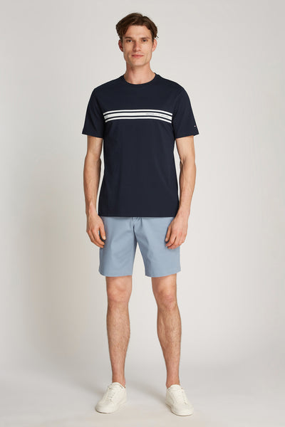 T-shirt bleu à manches courtes de TOMMY HILFIGER, avec trois rayures horizontales, porté avec un short bleu clair et des baskets blanches.