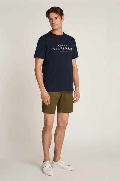 T-shirt bleu à manches courtes de TOMMY HILFIGER, porté avec un short vert olive et des baskets blanches.
