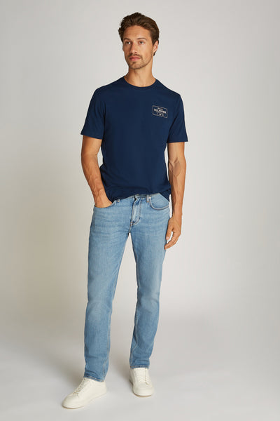 T-shirt à manches courtes bleu de TOMMY HILFIGER, porté avec un jean délavé et des baskets blanches.