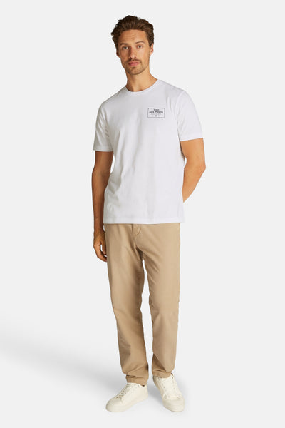 T-shirt blanc à manches courtes de TOMMY HILFIGER, avec un logo graphique discret, porté avec un pantalon chino beige.