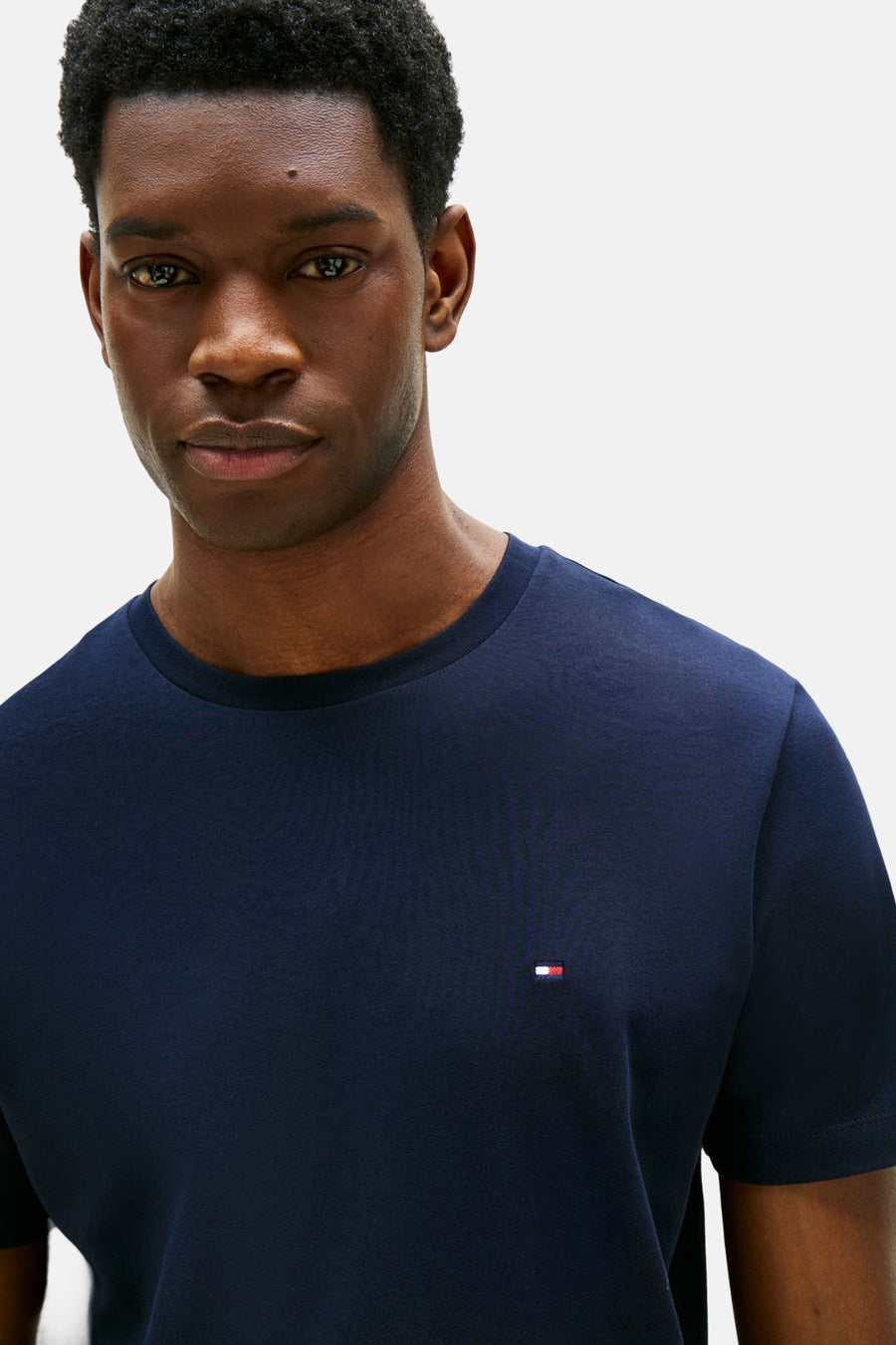 T-shirt bleu à manches courtes de TOMMY HILFIGER, porté par un homme à la peau foncée.