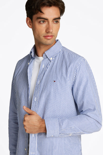 Chemise à rayures bleues de TOMMY HILFIGER, portée sur un t-shirt blanc, avec le logo sur la poitrine.