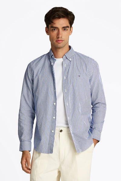Blauw gestreept overhemd met lange mouwen van Tommy Hilfiger, open gedragen over een wit T-shirt, met een beige broek.