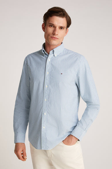 Chemise à manches longues verte rayée de Tommy Hilfiger, portée par un homme, avec pantalon blanc.