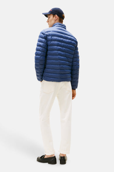 Veste courte bleue de TOMMY HILFIGER, matelassée avec des lignes horizontales, portée avec un pantalon blanc et des mocassins noirs.