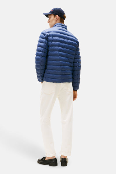 Veste courte bleue de TOMMY HILFIGER, matelassée avec des lignes horizontales, portée avec un pantalon blanc et des mocassins noirs.