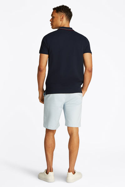Marineblaues Kurzarm-Poloshirt von TOMMY HILFIGER, getragen mit hellblauen Shorts und weißen Turnschuhen, Rückansicht.