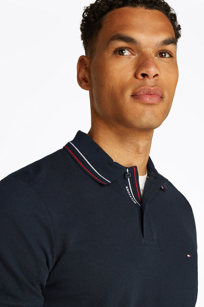 Polo à manches courtes bleu de TOMMY HILFIGER, avec col rayé rouge et blanc.