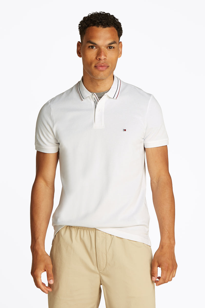 Wit poloshirt met korte mouwen van TOMMY HILFIGER, met gestreepte kraag en kenmerkend logo, gedragen met een beige broek.