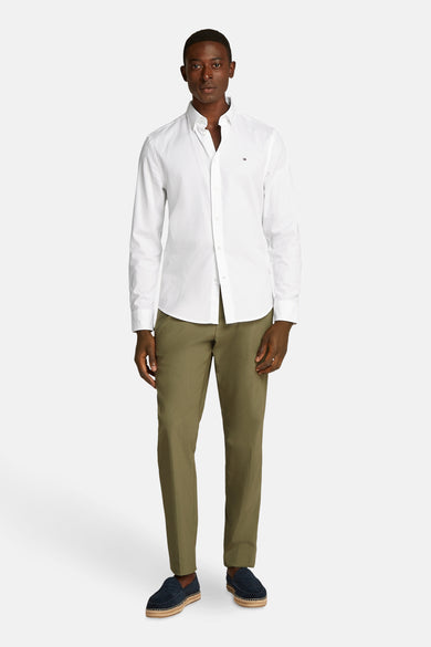Chemise blanche à manches longues de TOMMY HILFIGER, portée avec un pantalon kaki et des espadrilles.