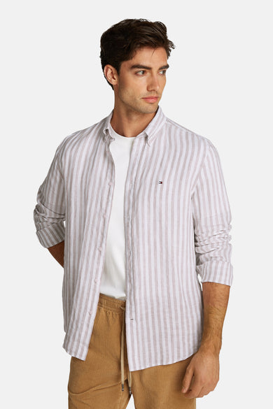 Chemise à manches longues beige rayée de TOMMY HILFIGER, portée ouverte sur un t-shirt blanc et un pantalon en velours côtelé.