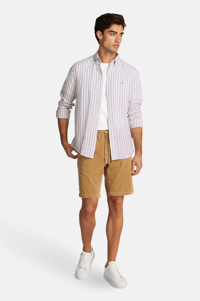 Chemise à manches longues beige à rayures, de TOMMY HILFIGER, portée sur un t-shirt blanc uni et un short marron.