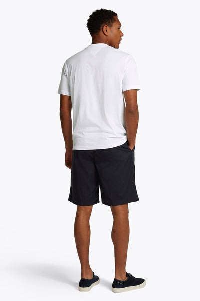 T-shirt à manches courtes blanc de Tommy Hilfiger, porté avec un short bleu marine et des chaussures de sport bleu marine.