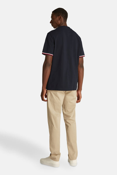 T-shirt à manches courtes bleu foncé de TOMMY HILFIGER avec rayures sur les manches, porté avec un pantalon beige et des baskets.