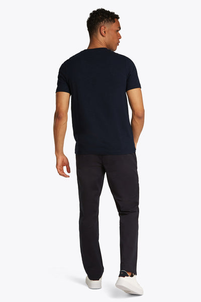 Donkerblauwe T-shirt met korte mouwen van TOMMY HILFIGER, gedragen met een zwarte broek en witte sneakers.